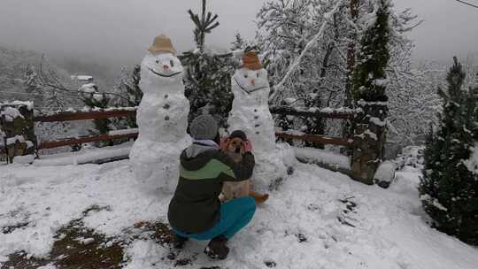 一个女人和她的狗和两个雪人摆姿势拍照