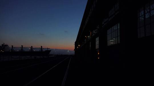 傍晚一艘大型货船靠近港口处大型仓库的宽镜头