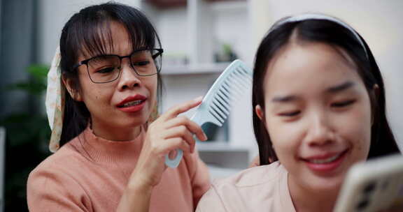 一位母亲正在给女儿梳头，她一边说话一边看