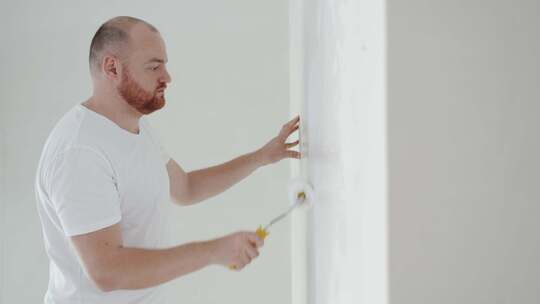 一个年轻人的特写镜头用白漆滚筒粉刷墙壁。家庭装修的概念视频素材模板下载