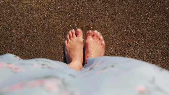 女性脚在水附近的沙滩上。