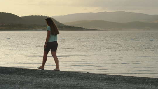 一个年轻的女人沿着山湖的岸边漫步。夕阳西