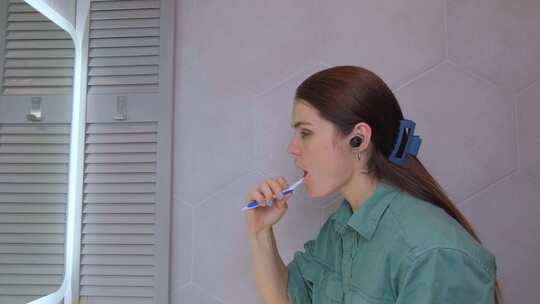 年轻女子在浴室里用无线耳机刷牙和听音乐