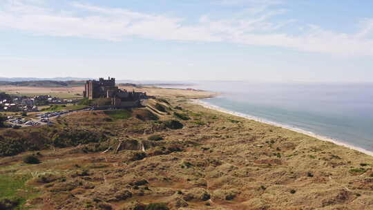 空中拍摄升起沙丘，露出海边一座美丽的城堡，度假者在上面