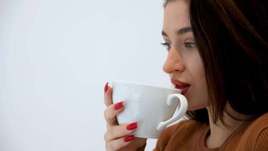 肖像红指甲的女人在诊所用白色杯子轻轻喝咖