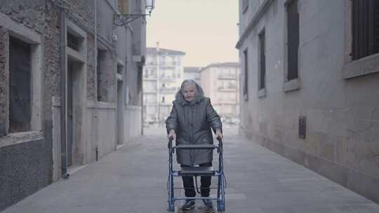 带助行器的老年妇女在沥青上用她的轮子在城