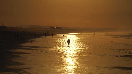 男人在金色繁忙的海滩上走向相机-背光广角