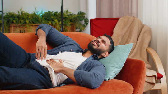印度男子躺在沙发上感觉突然强烈腹部胃痛胃视频素材模板下载