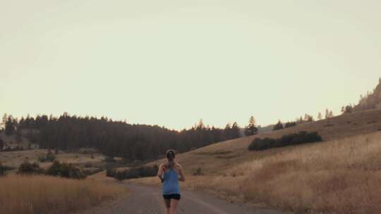 早上，一个女人沿着田野之间的土路向山上跑