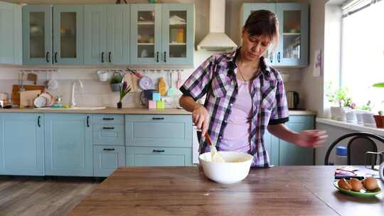 一个女人在家厨房准备食物，在碗里搅拌面团