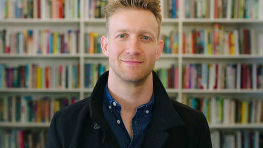 一个快乐的男性图书管理员，喜欢他的工作，微笑着站在书前视频素材模板下载