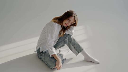 穿着休闲牛仔裤和白衬衫的年轻女子坐在地板