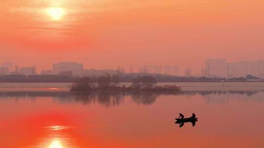 夕阳下的湖面小船剪影及岸上城市建筑剪影