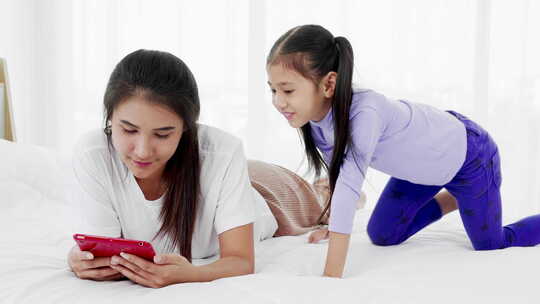白天玩平板电脑时，母亲和小孩躺在床上视频素材模板下载