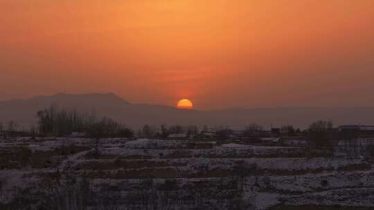 北方冬天高原雪后宁静村庄的橙色日落
