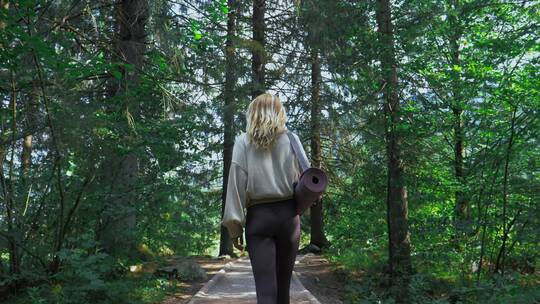 女人拿着瑜伽垫走在树林里