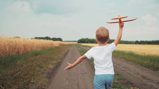 小男孩拿着玩具飞机在田间小路上奔跑
