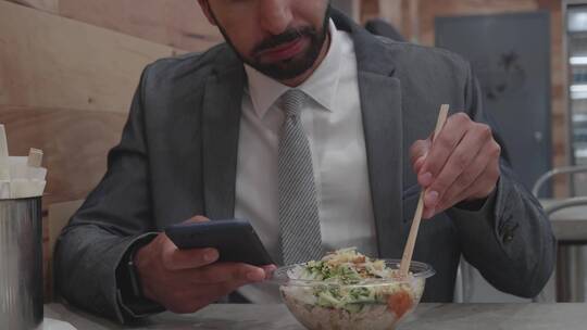 男商人边看手机边吃饭