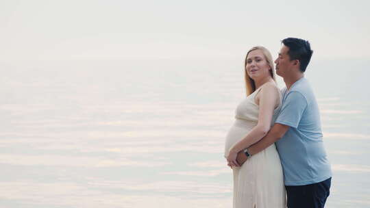 一名年轻的亚洲男子在海上日落背景下拥抱他怀孕的妻子