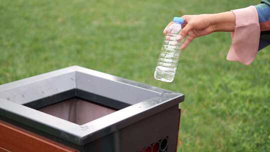 妇女将空塑料水瓶扔进垃圾桶或垃圾桶
