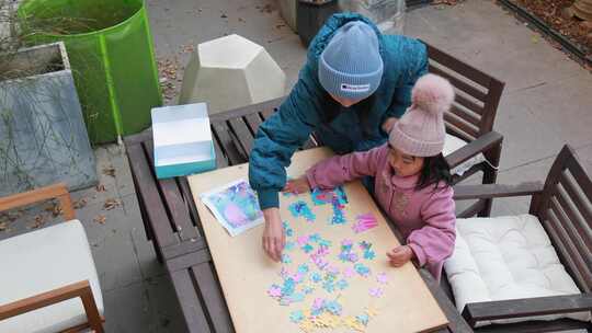 妈妈与女儿在别墅院子木桌子上玩拼图