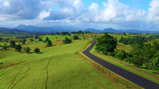 澳大利亚高原阿瑟顿白天穿过绿色山丘的空沥青路。-空中拉力视频素材模板下载