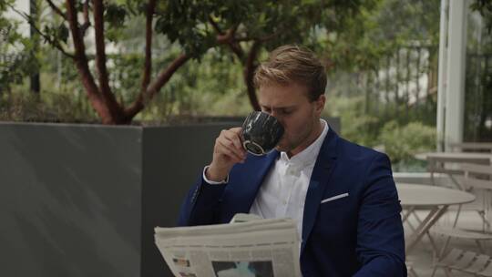 商人坐在户外看报纸喝咖啡