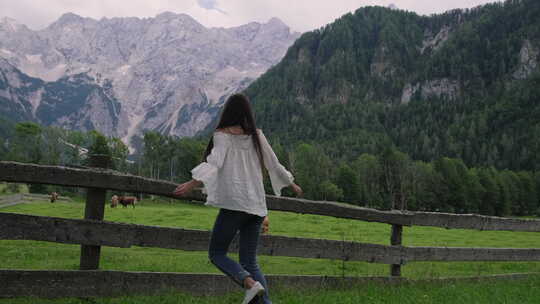 年轻女子在阿尔卑斯山和农场附近的草地上跳跃和旋转