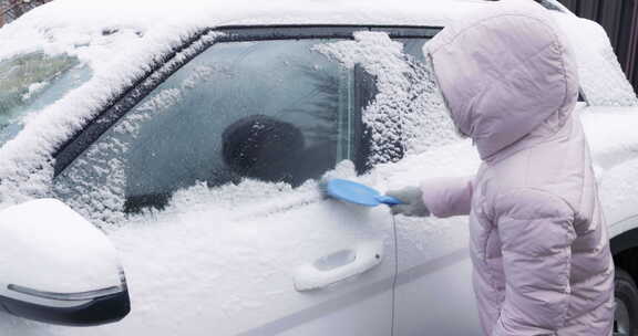 女人用刷子清理雪地上的汽车