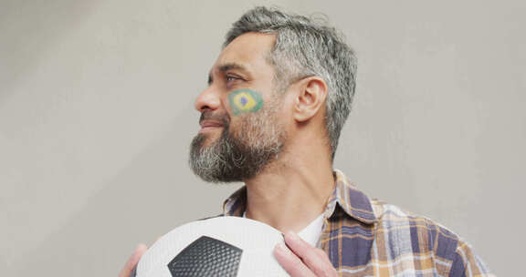 脸颊上插着巴西国旗的快乐混血儿拿着足球