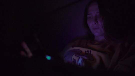 一个女人晚上在床上玩手机，脸上有屏幕反射