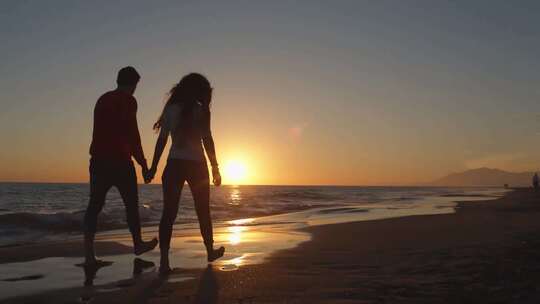 年轻的夫妇在夕阳下手牵手沿着海滩散步
