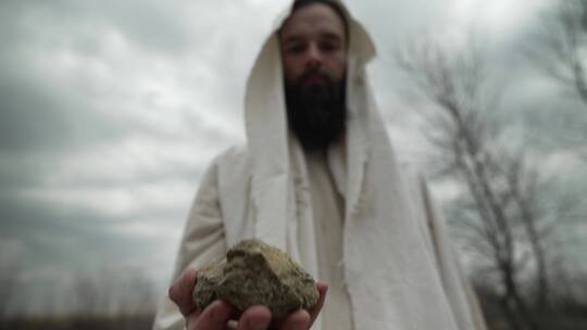 森林中穿着白色长袍的基督教信徒拿着一块石头视频素材模板下载