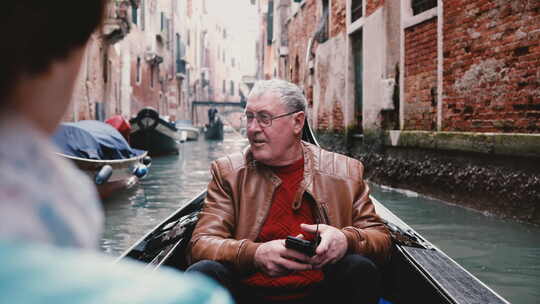 快乐的欧洲资深男旅行者在贡多拉兴奋，享受威尼斯运河之旅