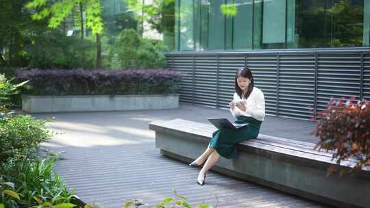 职业女性户外使用笔记本电脑和手机办公