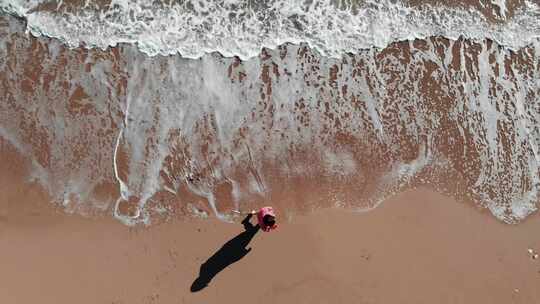 穿着红色连衣裙的女孩走在沙滩上，白色的波浪溅起白色的泡沫视频素材模板下载