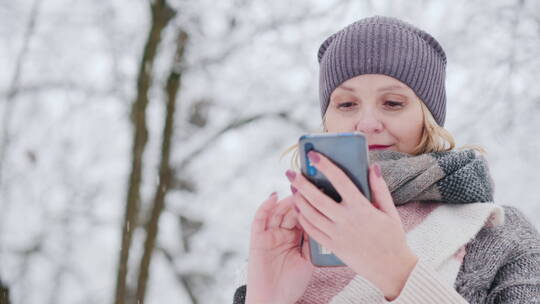 年轻女子在下雪的公园使用智能手机