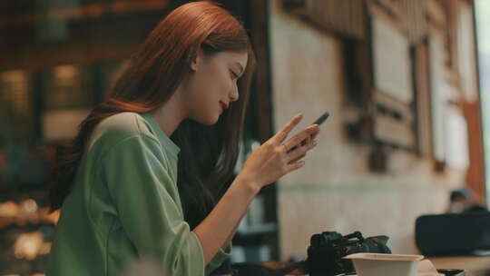 年轻的亚洲女性坐在咖啡店用智能手机浏览互联网，在手机上聊天