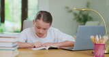 桌子上专注的少女用手指读一本书笔记本电脑旁边的跟踪线高清在线视频素材下载