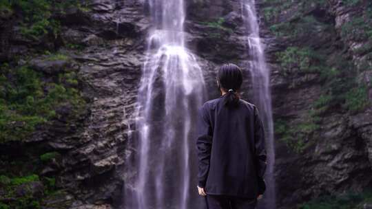 女性游客背影面向山水感受亲近自然山峰瀑布