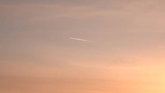 夕阳下天空中拉线的飞机飞过