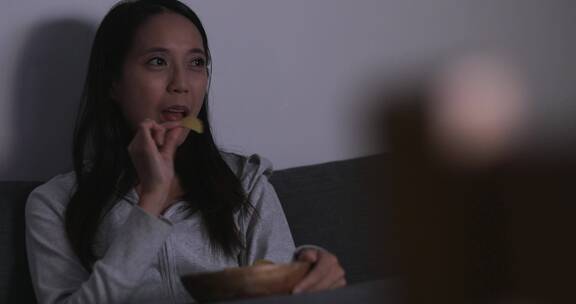 女人坐在沙发上吃着薯片追剧