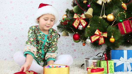 戴着圣诞帽的孩子坐在圣诞树旁扔彩纸