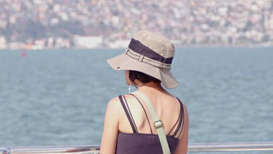 戴帽子的年轻女游客在船上观看海洋