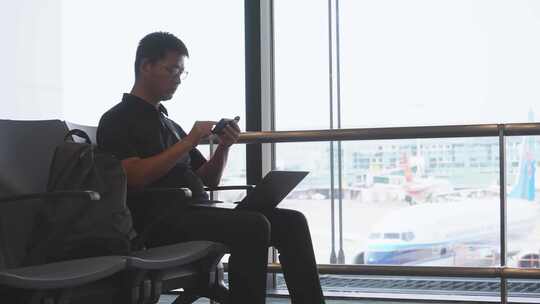 商务男子在机场使用笔记本电脑和手机工作