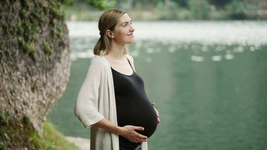 孕妇站在山湖附近轻轻抚摸肚子