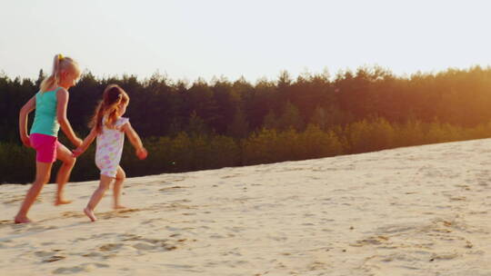 日落两个快乐的女孩在沙滩奔跑