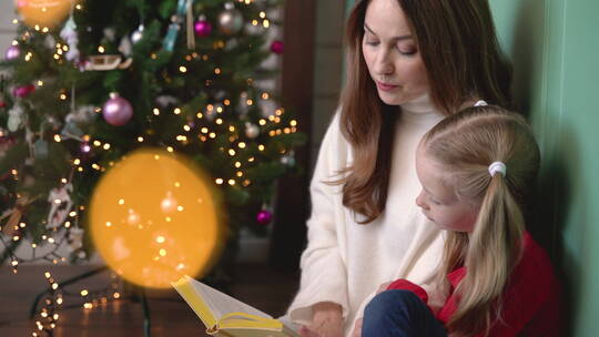 坐在圣诞树旁看书的母女视频素材模板下载