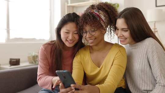三个多种族的女性朋友在家里玩手机