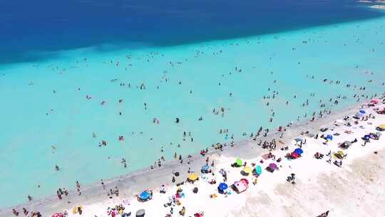 人们在清澈的热带绿松石浅蓝色大海的白色沙滩上度假游泳